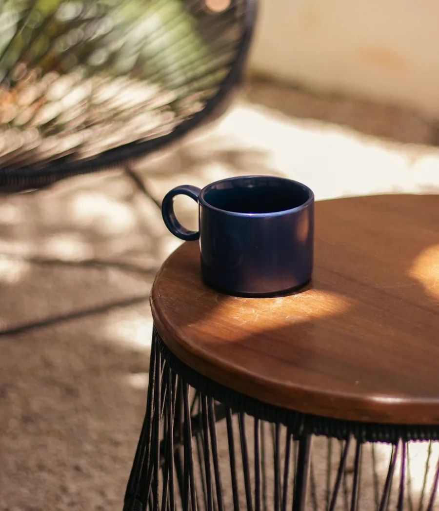 A blue cup on a wooden side table in the sun